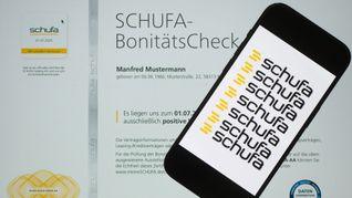 Ein Smartphone mit dem Logo der Wirtschaftsauskunftei Schufa liegt auf einem Display mit einem Musterdokument eines Schufa-Bonitätszertifikat.